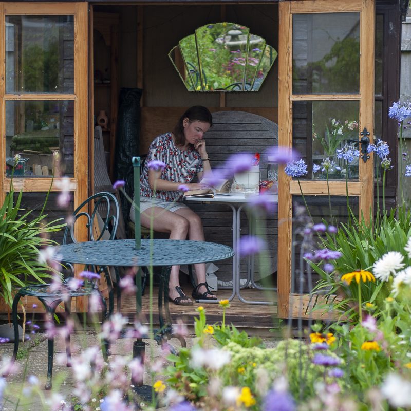 A woman reading in a summer house with garden flowers in the foreground
