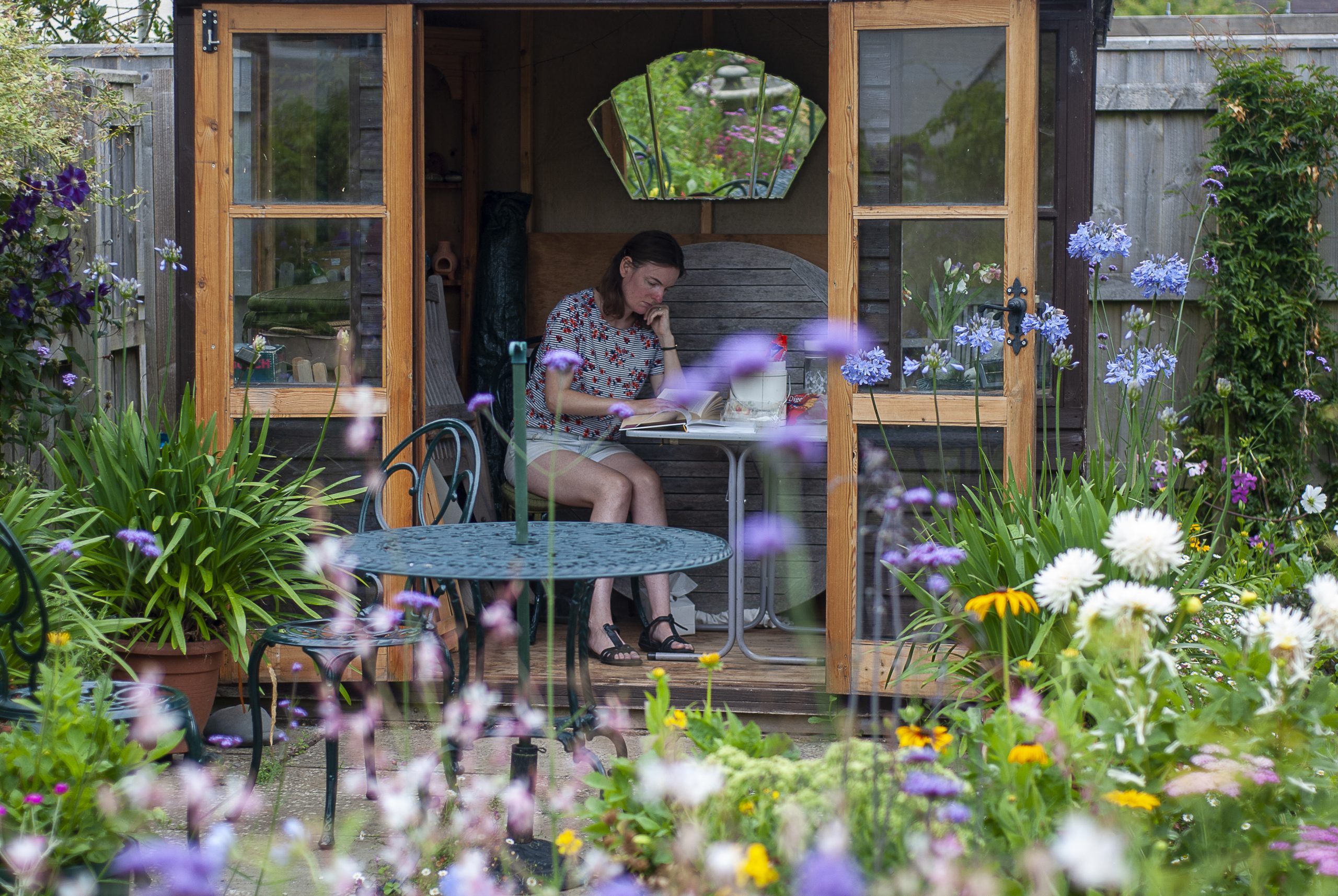 A woman reading in a summer house with garden flowers in the foreground