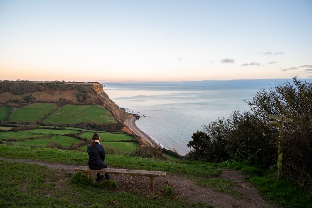 Photo of a woman sat on a bench looking out to sea in Sidmouth